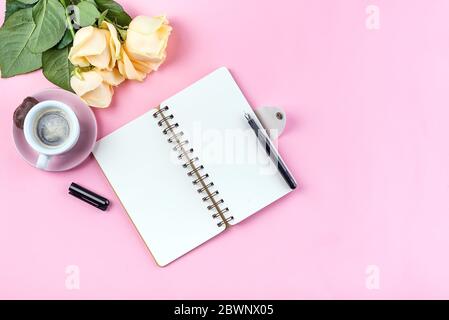 Morgen Kaffee Tasse zum Frühstück, leere Notizbuch, Bleistift und Rose auf rosa Tischansicht . Frau am Schreibtisch. Stockfoto