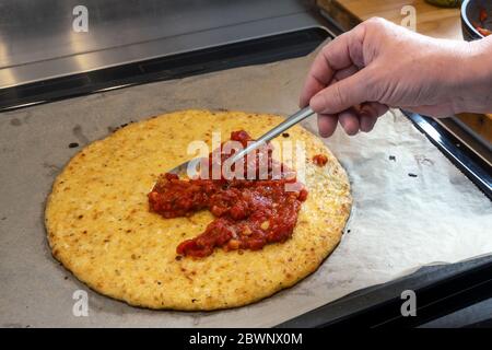 Hand verteilt Tomatensauce auf einer Pizzabruste aus zerkleinerten Blumenkohl, Kochen eine gesunde Alternative für Abnehmen mit Low Carb oder ketogene Ernährung, Stockfoto