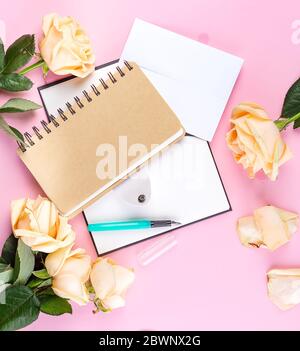 Draufsicht von Spiral-Kraftpapier Notizbuch und beigen Rosen isoliert auf rosa Hintergrund für Mockup Stockfoto