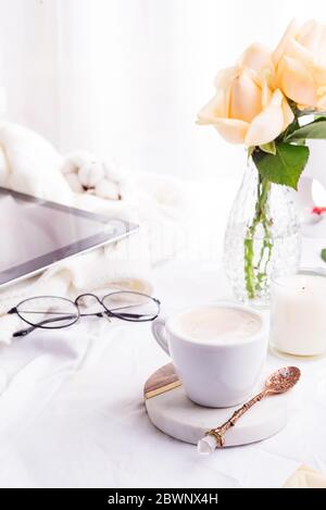 Tablet pc Computer, Kaffeetasse und beigefarbene Rosen am Morgen auf dem weißen Betthintergrund, flach gelegt Stockfoto