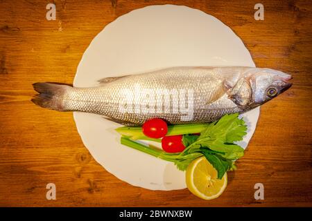 Seebarsch, Zitrone, Sellerie und Tomaten auf Holzhintergrund Stockfoto