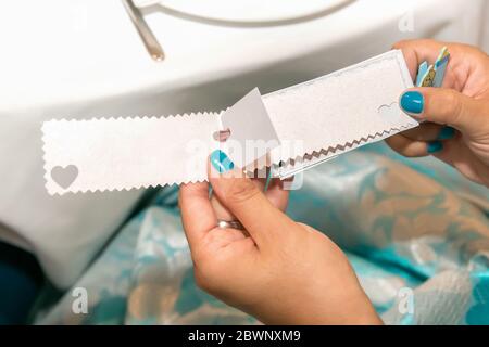 Kleiner Bogen auf einer Karte mit Kopierraum, der von den Händen einer Frau gehalten wird, mit ihren blauen Nägeln. Stockfoto