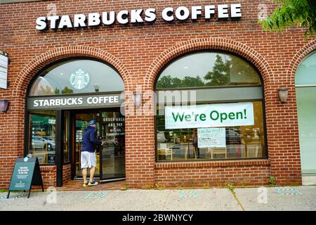 Mount Kisco, New York 29. Mai 2020: Als Westchester County NY Phase 1 der Wiedereröffnung beginnt, nachdem es aufgrund der Coronavirus-Pandemie eine Pause eingelegt hat, bietet Starbucks eine mobile Bestellabholung mit einem großen Schild mit der Aufschrift "Wir sind offen!" an. Quadrate außen zeigen 6 Fuß soziale Distanzierung.EIN Mann betritt den Laden. Stockfoto