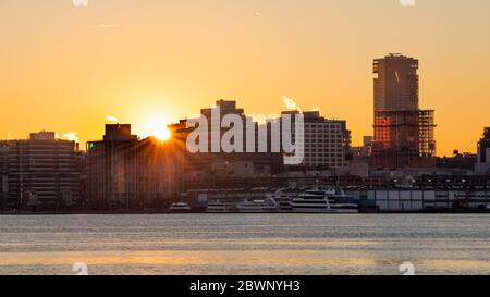 Die Sonne bricht bei Sonnenaufgang hinter einer Reihe von Gebäuden in New York durch Stockfoto