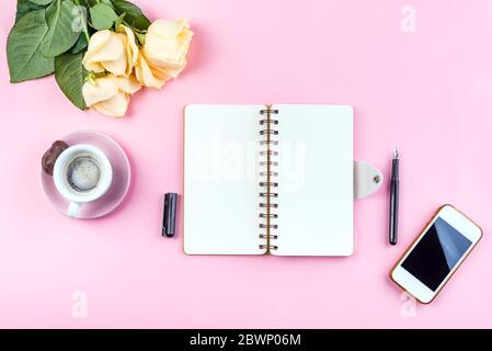 Morgen Kaffee Tasse zum Frühstück, Telefon, Notizbuch, Bleistift und Rose auf rosa Tisch Top-Ansicht . Frau am Schreibtisch. Stockfoto