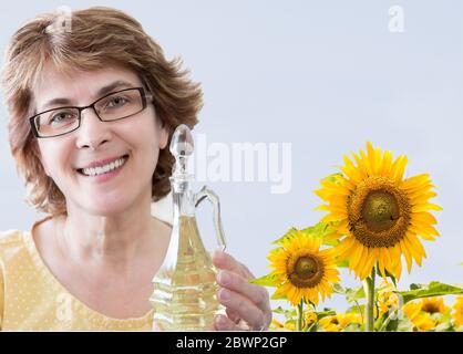 Horizontale Nahaufnahme von kaukasischer Frau in einem Sonnenblumenfeld, das eine Flasche Sonnenblumenöl hält. Stockfoto