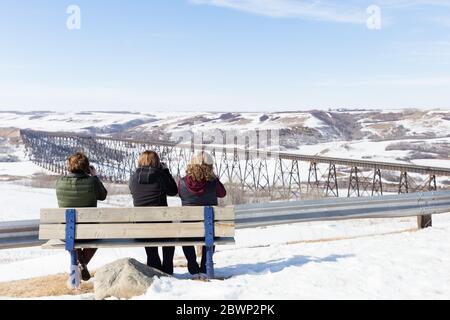 Horizontale Aufnahme von drei Frauen, die im Winter auf einer Bank sitzen und die Szene vor ihnen fotografieren. Stockfoto