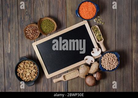 Sortiment aus Hülsenfrüchten, Linsen, Chikpea und Bohnen von oben. Zusammensetzung von verschiedenen Arten von Hülsenfrüchten in Schalen auf Holzhintergrund. Schwarze Tafel mit Stockfoto