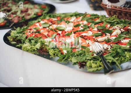 Vegetarischer Salat mit Tomaten, Mozzarella und Salat auf Edelstahltablett auf Büfetttisch. Feier, Party, Geburtstag oder Hochzeit Konzept. Stockfoto