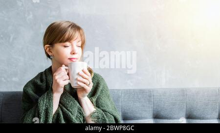 Fröhliches Mädchen zu Hause hält eine Tasse, genießen inhaliert das Aroma des Drink.Homeliness, glückliches Zuhause bleiben und Kaffee am Morgen Konzept Stockfoto