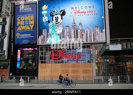 Ein Paar mit Masken fährt mit dem Fahrrad an den Fenstern des Disney-Stores im Times Square vorbei, wo nach einer weiteren Nacht des Vandalismus und Plünderer, die die Proteste gegen den Tod von George Floyd als Gelegenheit nutzen, Chaos zu verursachen, an Bord ging. Manhattan, New York City, USA 2. Juni 2020 Stockfoto