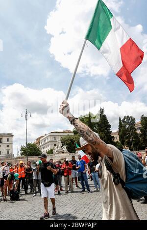 Rom, Italien. Juni 2020. Ein Protestler spricht, während ein anderer mit einer dreifarbigen italienischen Flagge während einer Demonstration, an der die Bewegung der Orange Vests (Gilet Arancioni) während eines Protestes gegen die italienische Regierung teilnahm, geht. Die Bewegung der Orangen Westen versammelt mehrere Gruppen von Koronavirus-Leugnern, Verschwörungstheoretikern, rechtsextremen Sympathisanten und einfachen Menschen, die unter den wirtschaftlichen Auswirkungen der von der Regierung auferlegten Blockade zur Eindämmung der Covid-19-Pandemie leiden. Kredit: Riccardo De Luca - Update Images/Alamy Live News Stockfoto