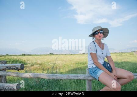 Junge Frau in einem Sonnenhut sitzend und posiert auf Ein geteilter Schienenzaun auf einer Ranch Stockfoto