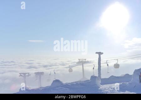 Die Sonne erleuchtet hinter diesen Gondel- und T-Bar-Skiliften, während sie unter den rollenden Wolken, gefroren in Schnee und Eis, aufsteigen. Hart und kalt. Stockfoto