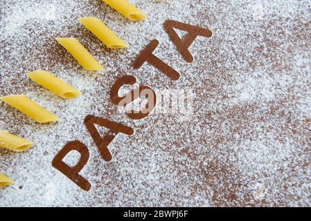Holzhintergrund mit bestreut Mehl und das Wort Pasta geschrieben. Stockfoto