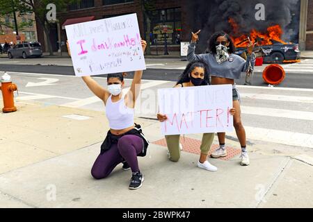 Drei Frauen posieren mit Schildern vor zwei brennenden Polizeiautos in der Innenstadt von Cleveland, Ohio, USA während eines Protestes zu Black Lives Matter am 30. Mai 2020. Die drei waren unter Tausenden, die in Cleveland auf die Straßen gingen, um gegen die Polizeipolitik, die Praktiken und die Ermordung schwarzer Menschen zu protestieren. Stockfoto