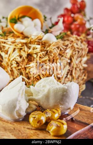 Fresca Mozzarella mit Knoblauch und geräucherten Oliven auf einem Holzständer auf grau-blauem Hintergrund. Italienischer Käse. Stockfoto