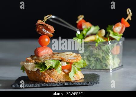 Nahaufnahme eines schmackhaften offenen Sandwich mit Käse, Fleisch und Gemüse mit einem unscharf Edelstahl Servierkorb mit Gemüse Stockfoto