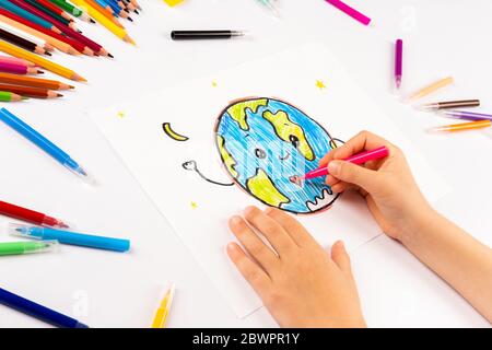 Kind Mädchen zeichnet Planeten Erde auf einem weißen Blatt. Stockfoto