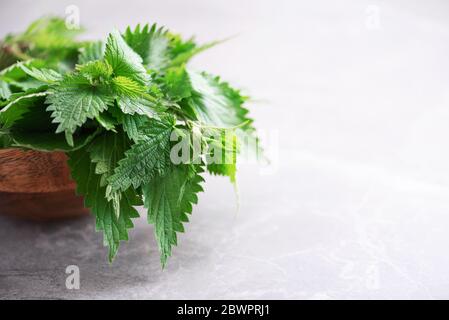 Brennnesseln, urtica. Grüne Brennnessel Blätter in Holztopf auf grauem Hintergrund. Alternative pflanzliche Medizin. Pflege für Hautallergien. Naturheilkunde, ganzheitlich Stockfoto