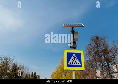 Das Fußgängerübergangsschild mit Solarpaneelen, die oben installiert sind. Verkehrszeichen und Regeln. Stockfoto