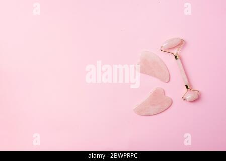 Rosa gua Sha Gesichtsmassage Roller. Anti-Age-, Lifting-, Straffung Gesicht Behandlung zu Hause. Hautpflege Konzept. Rose Quarz Steinrolle auf rosa Hintergrund. Stockfoto