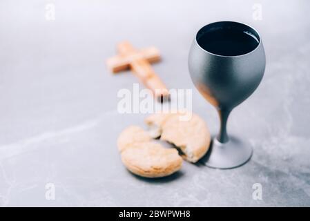 Ungesäuertes Brot, Kelch mit Wein, Holzkreuz auf grauem Hintergrund. Christliche Kommunion zur Erinnerung an das Opfer Jesu. Osterpassah. Eucharistie Stockfoto