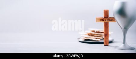 Matzos ungesäuertes Brot, Kelch Wein, Holzkreuz auf grauem Hintergrund. Christliche Kommunion zur Erinnerung an das Opfer Jesu. Osterpassah Stockfoto