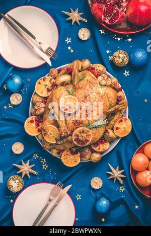 New Year Dinner Tisch. Gebratenes Weihnachts-Huhn mit Orangenscheiben, Cranberries, Knoblauch, festliche Dekoration, Kerzen, Mandarine, Granatapfel, Gold Stockfoto