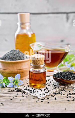 Nigella Sativa Öl in Fläschchen, Sauceboat und Flasche, Samen in einem Löffel und schwarzem Kreuzkümmelmehl in einer Schüssel auf Burlap, kalingi Zweige mit blauen Blumen und lea Stockfoto