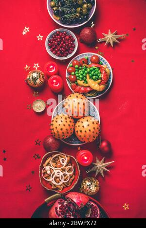 Vegane Weihnachts-Vorspeisen, Oliven, Orangen, Obst, Gemüsesalate, Kerzen, Mandarine, Granatapfel, Sternglitzern funkeln auf rotem Grund. Oben Stockfoto