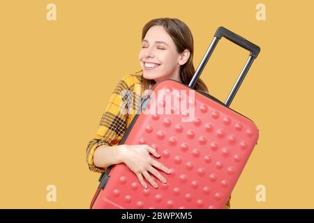 Glückliches junges Mädchen mit geschlossenen Augen umarmt einen Koffer. Stockfoto