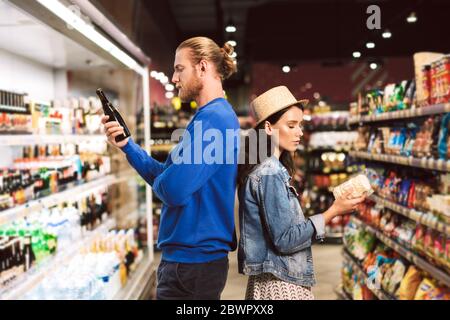 Junge schöne Paar stehen zurück an Rücken nachdenklich Auswahl Produkte während Sie Zeit in modernen Supermarkt Stockfoto