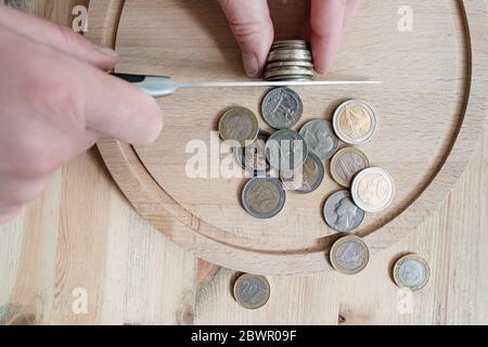 Die Hände schneiden Euro- und Dollarmünzen mit einem Messer, trennen sie wie Lebensmittelstücke. Konzept von Steuern, Betrug oder Gewinn. Draufsicht. Stockfoto