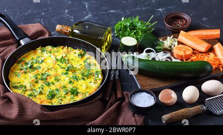 Gesundes Frühstück: Gemüse- und Hühnereier Frittata aus zerfetzten Zucchini und Karotte auf einer Bratpfanne auf dunklem Betongrund mit Oliv serviert Stockfoto