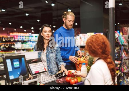 Junge schöne Paar in der Nähe der Kasse beim Kauf von Produkten zusammen in modernen Supermarkt Stockfoto