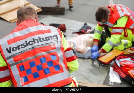 27. Mai 2020, Sachsen, Leipzig: Ein Sanitäter mit "Vorsicht" auf dem Rücken behandelt eine verletzte Person während einer Übung. Während der Übung wurde eine spezielle Tasche für sogenannte "Massenunfall- und Krankheitsfälle" (MANV) vorgestellt. Es enthält unter anderem spezielle Verbandbinden zur Blutungsunterbindung bei schweren äußeren und inneren Verletzungen sowie Markierungen für Menschen mit unterschiedlichem Schweregrad. Bei einem Massenunfall sind zunächst nur wenige Rettungsteams mit einer großen Anzahl von Verletzten konfrontiert. Das Überleben von möglichst vielen Patienten kann durch gewährleistet werden Stockfoto