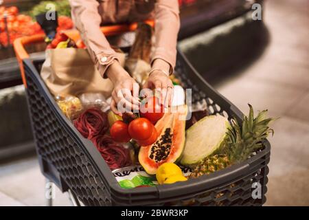 Nahaufnahme Frau Hände hält Tomaten in Trolley voller frischer Produkte in modernen Supermarkt isoliert Stockfoto