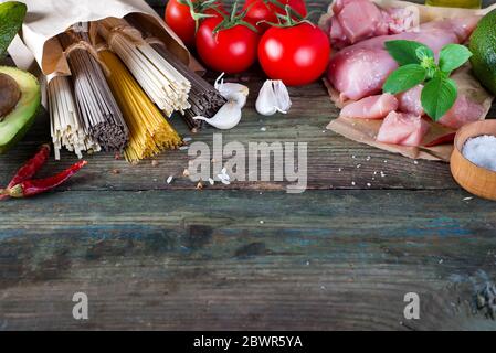 Bündel der Italienische Spaghetti, raw Soba Nudeln und comen, Huhn, rohes Fleisch, Avocado mit Tomaten auf einem alten Holz- Hintergrund, flay legte sich zu kopieren. C Stockfoto