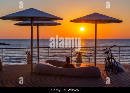 Blick auf Sonnenschirmen und ruhenden Radfahrer auf Promenade bei Sonnenuntergang, Hayarkon Street, Tel Aviv, Israel, Naher Osten Stockfoto