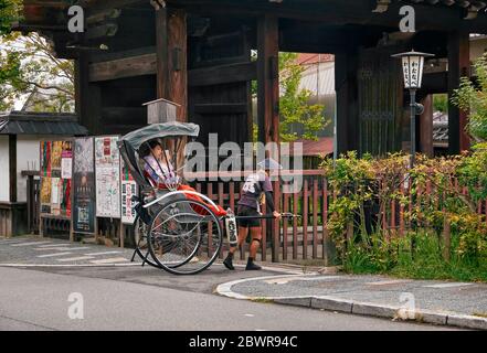 KYOTO, JAPAN - 18. OKTOBER 2019: Eine gezogene Rikscha (oder Rickscha) fährt einen zweirädrigen Passagierwagen mit Touristen, die als Maiko auf der Straße gekleidet sind Stockfoto