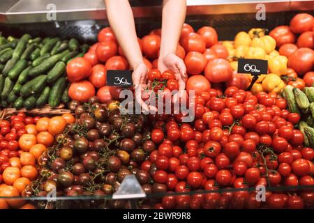 Nahaufnahme Verkäufer hält Tomaten mit Vielfalt an Gemüse in modernen Supermarkt Stockfoto