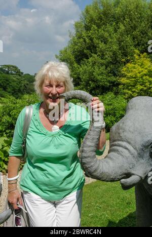 Ältere Frau, die den Rüssel einer Skulptur eines indischen Elefanten in den Gärten des Sezincote House, Gloucestershire, Großbritannien, hält Stockfoto