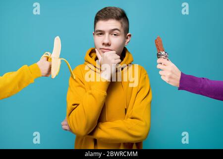 Junger Mann, der zwischen Schokoriegel und Banane wählen kann Stockfoto