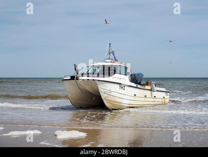 Ein modernes Krabbenboot im Katamaranstil an Land am Cromer Beach, Norfolk wartet darauf, nach einer erfolgreichen Reise mit dem Traktor über die Gezeitenlinie gezogen zu werden. Stockfoto