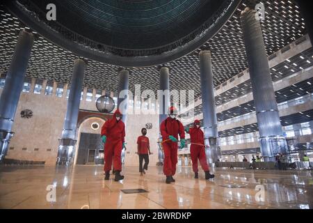 Jakarta, Indonesien. Juni 2020. Feuerwehrleute tragen Schutzanzüge und sprühen Desinfektionsmittel im Komplex der Istiqlal Moschee in Jakarta, Indonesien, 3. Juni 2020. Kredit: Agung Kuncahya B./Xinhua/Alamy Live News Stockfoto