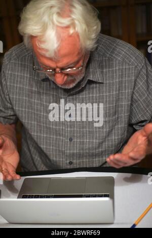 Porträt eines weißen bärtigen älteren Mannes mit grauem Hemd Blick auf einen Laptop, Notebook-Bildschirm. Stockfoto