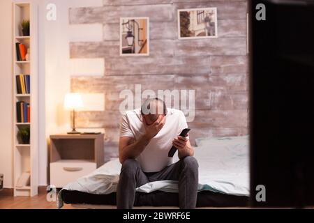 Fröhlicher Mann, der sein Gesicht bedeckt, während er nachts eine fernsehshow ansieht. Stockfoto