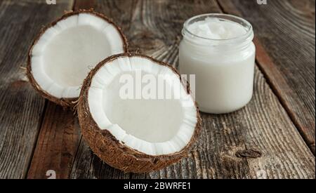 Zwei Hälften Kokosöl und Kokosöl in einem Glas auf einer Holzfläche. Das Konzept der gesunden Ernährung. Stockfoto