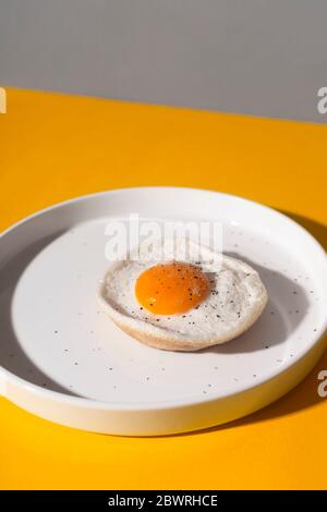 Spiegelei auf einem weißen Teller auf gelbem Hintergrund mit Schatten. Stockfoto